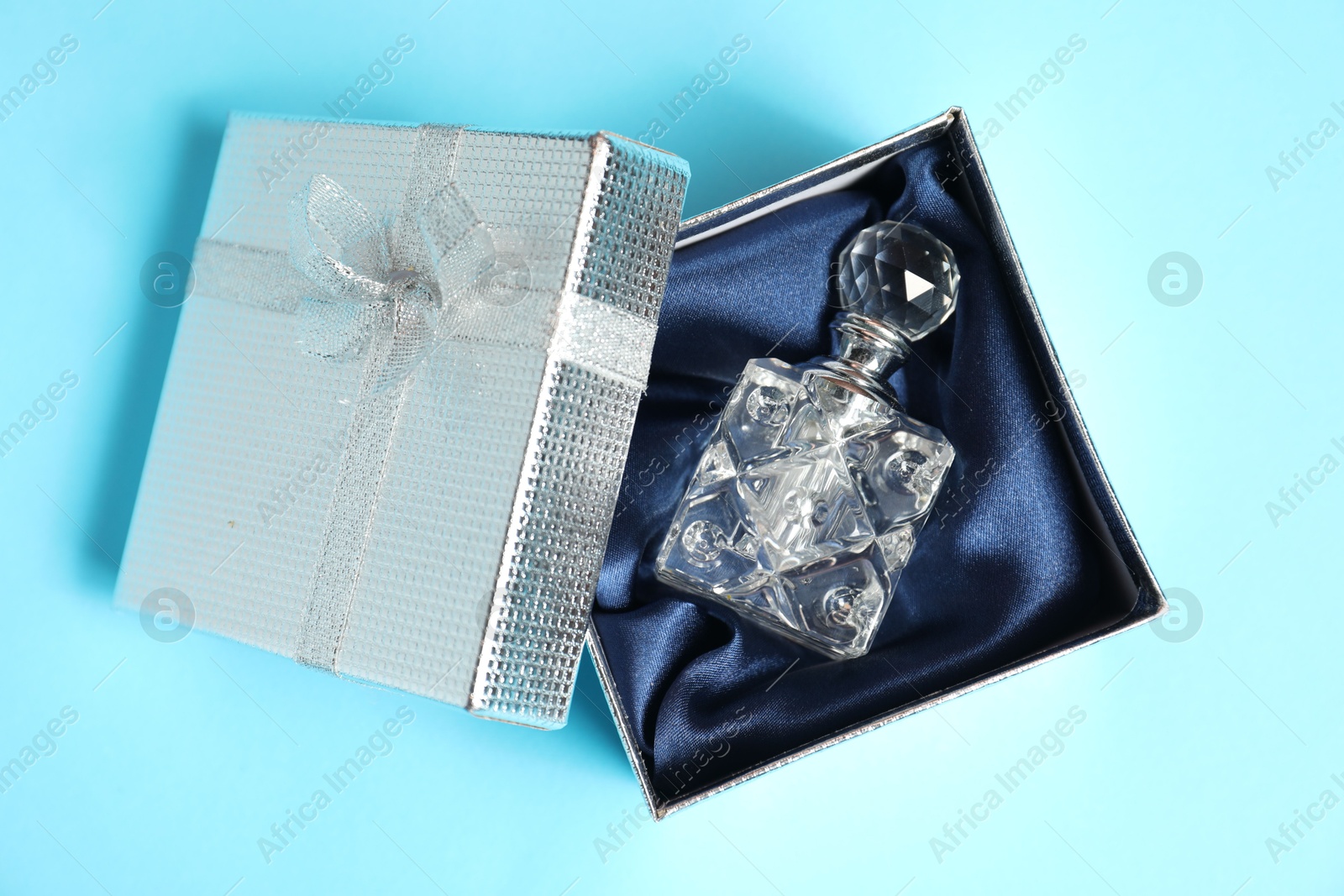 Photo of Perfume bottle in gift box on light blue background, top view