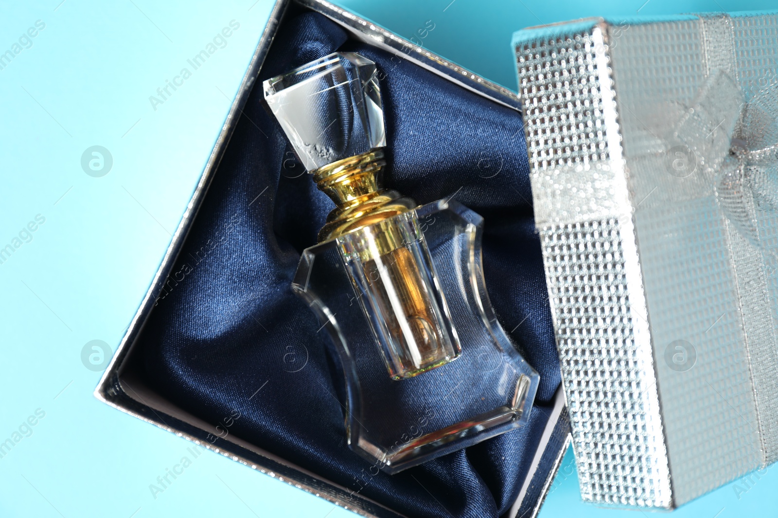 Photo of Perfume bottle in gift box on light blue background, top view