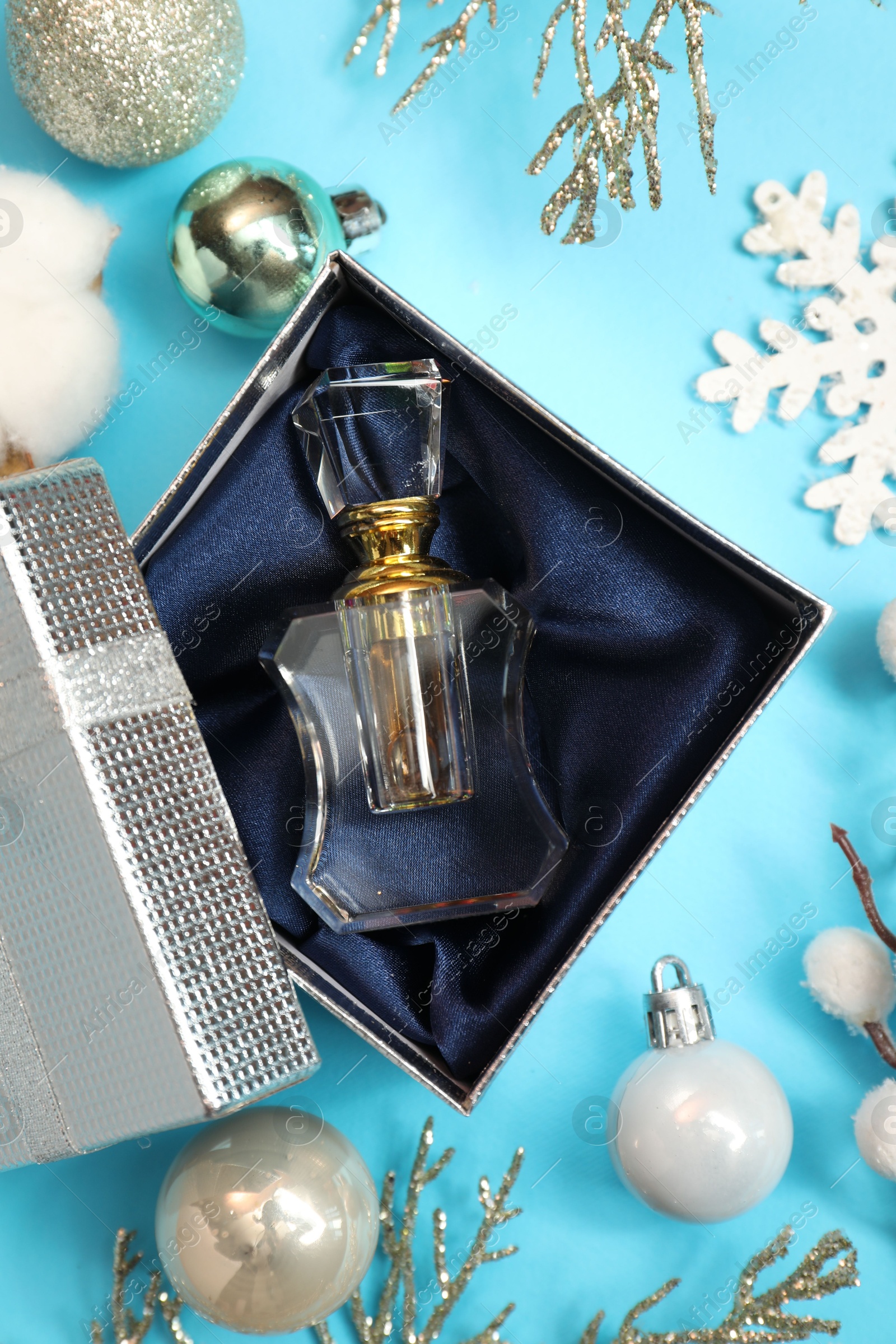 Photo of Perfume bottle in gift box and Christmas decor on light blue background, flat lay