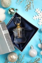 Perfume bottle in gift box and Christmas decor on light blue background, flat lay