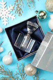 Photo of Perfume bottle in gift box and Christmas decor on light blue background, flat lay