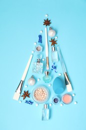 Photo of Christmas tree made of perfume bottles and makeup products on light blue background, flat lay