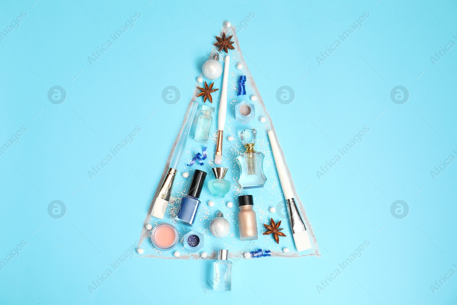 Photo of Christmas tree made of perfume bottles and makeup products on light blue background, flat lay