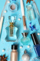 Perfume bottles and makeup products on light blue background, flat lay