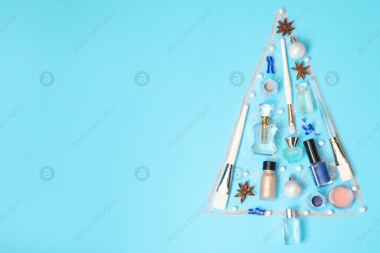 Photo of Christmas tree made of perfume bottles and makeup products on light blue background, flat lay. Space for text