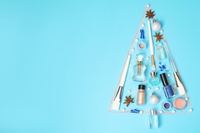 Christmas tree made of perfume bottles and makeup products on light blue background, flat lay. Space for text