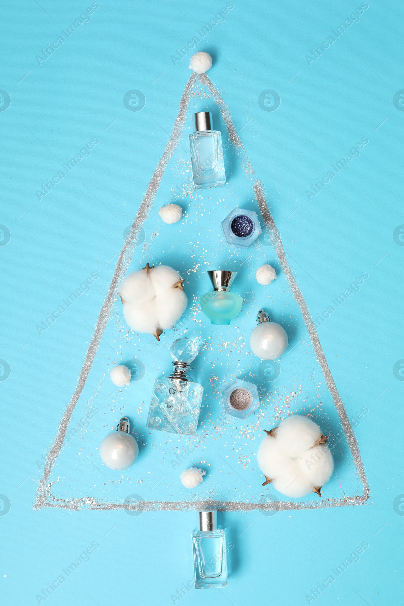 Photo of Christmas tree made of perfume bottles and cotton flowers on light blue background, flat lay