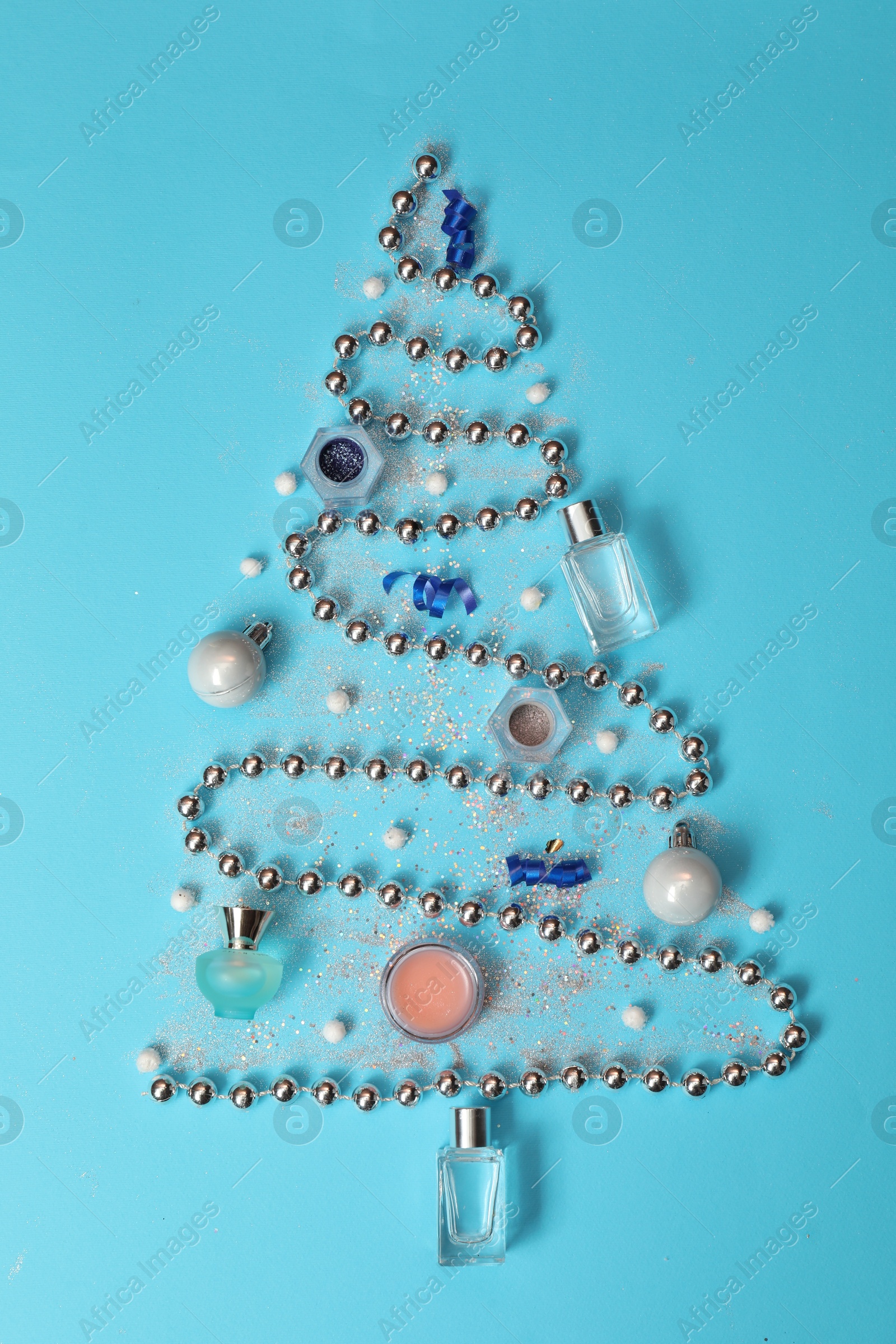 Photo of Christmas tree made of perfume bottles and makeup products on light blue background, flat lay