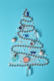 Photo of Christmas tree made of perfume bottles and makeup products on light blue background, flat lay