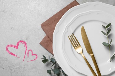 Image of Table setting for romantic Valentine's day celebration, top view. Plates, cutlery, eucalyptus branches and hearts on grey table