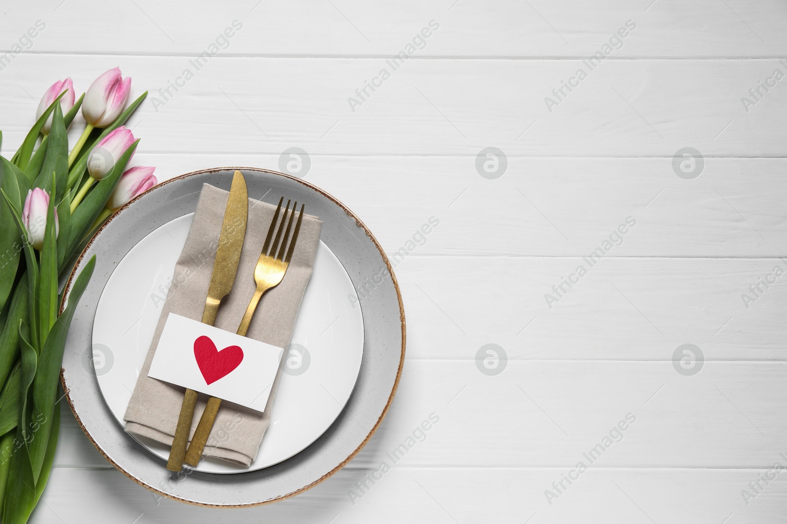 Image of Table setting for romantic Valentine's day celebration, top view. Plates, cutlery and flowers on white wooden table, space for text