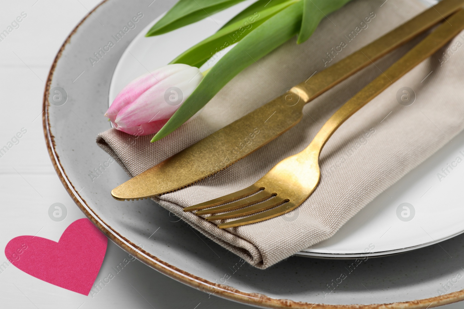 Image of Table setting for romantic Valentine's day celebration. Plates, cutlery, tulip and heart on white table, closeup