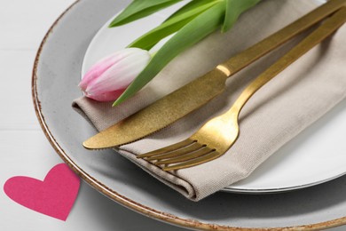 Table setting for romantic Valentine's day celebration. Plates, cutlery, tulip and heart on white table, closeup