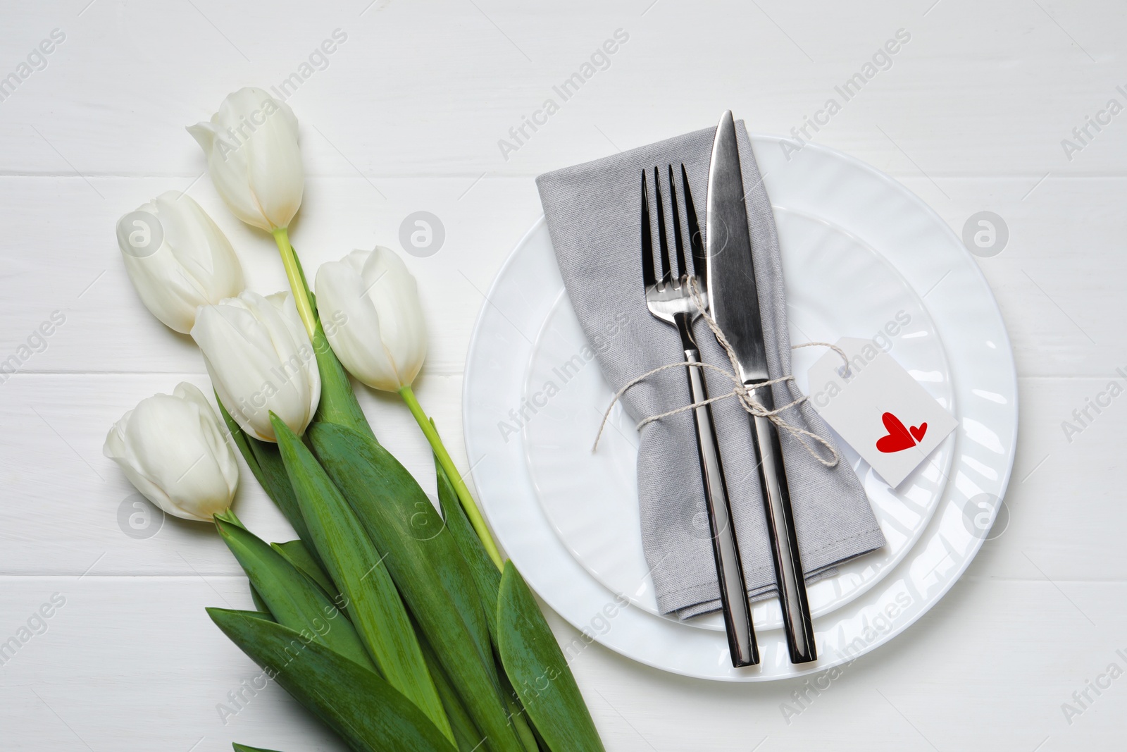 Image of Table setting for romantic Valentine's day celebration, top view. Plates, cutlery and flowers on white wooden table