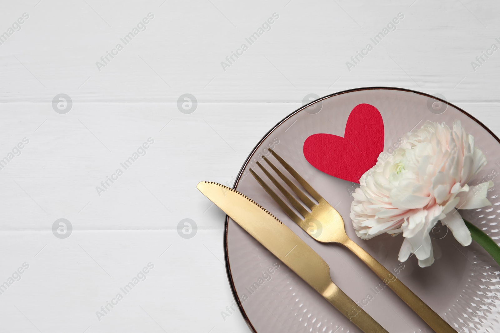 Image of Table setting for romantic Valentine's day celebration, top view. Plate, cutlery, flower and heart on white wooden table, space for text