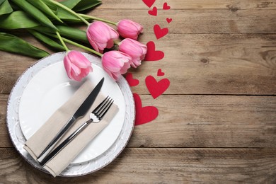 Image of Table setting for romantic Valentine's day celebration, top view. Plates, cutlery, flowers and hearts on wooden table, space for text