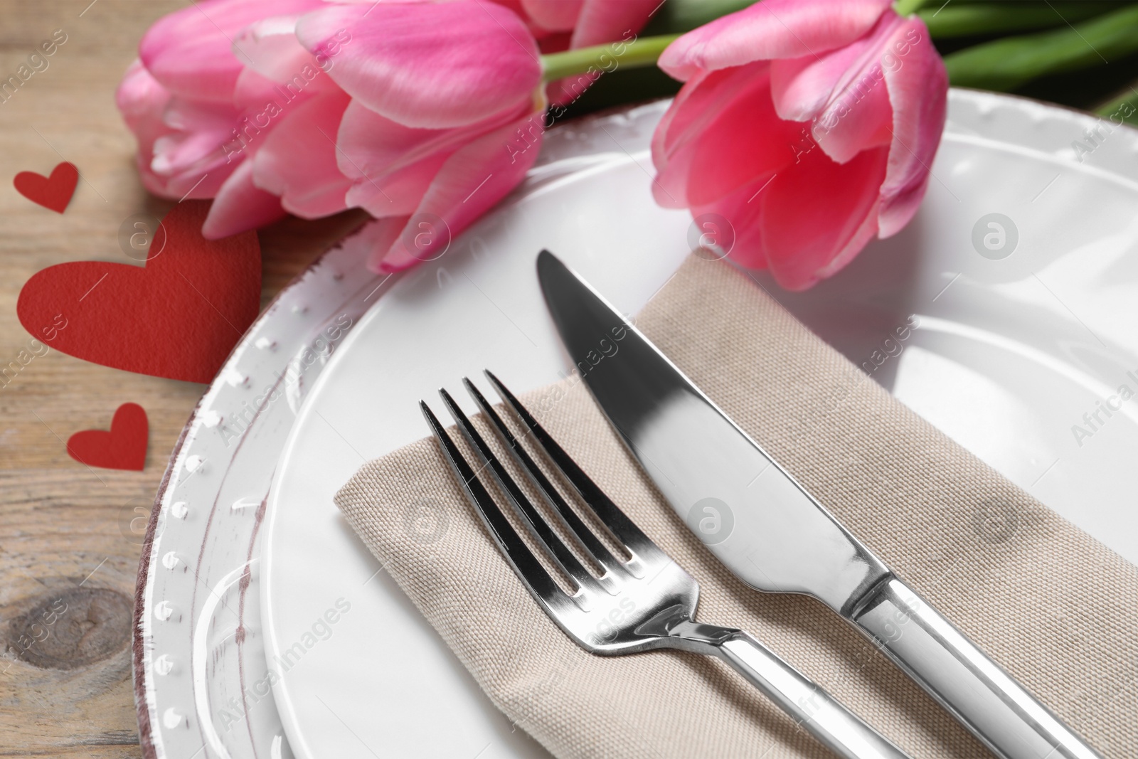 Image of Table setting for romantic Valentine's day celebration. Plates, cutlery, flowers and hearts on wooden table, closeup