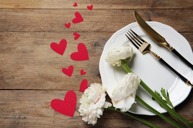 Image of Table setting for romantic Valentine's day celebration, top view. Plate, cutlery, flowers and hearts on wooden table, space for text