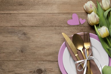 Image of Table setting for romantic Valentine's day celebration, top view. Plates, cutlery, flowers and hearts on wooden table, space for text