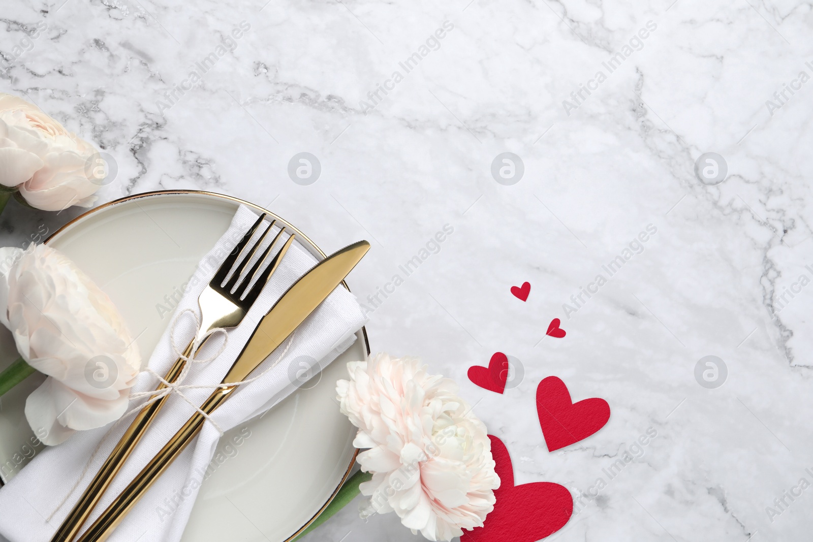 Image of Table setting for romantic Valentine's day celebration, top view. Plate, cutlery, flowers and hearts on white marble table, space for text