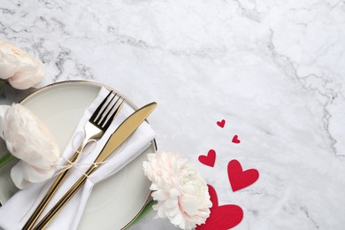 Image of Table setting for romantic Valentine's day celebration, top view. Plate, cutlery, flowers and hearts on white marble table, space for text