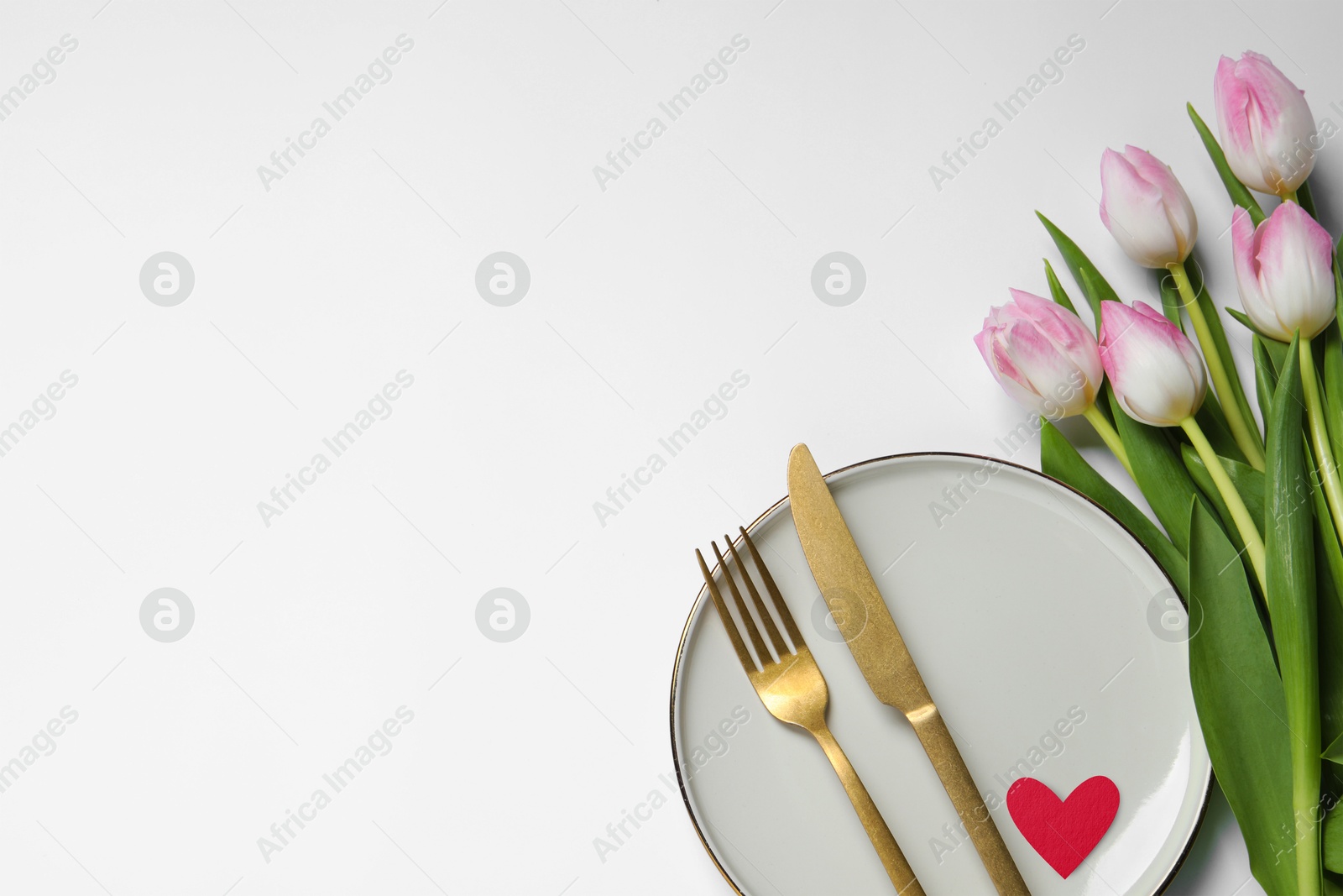 Image of Table setting for romantic Valentine's day celebration, top view. Plate, cutlery, heart and flowers on white table, space for text