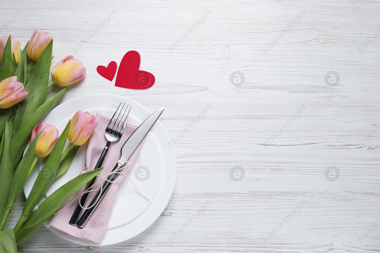 Image of Table setting for romantic Valentine's day celebration, top view. Plates, cutlery, flowers and hearts on white marble table, space for text