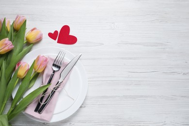 Image of Table setting for romantic Valentine's day celebration, top view. Plates, cutlery, flowers and hearts on white marble table, space for text