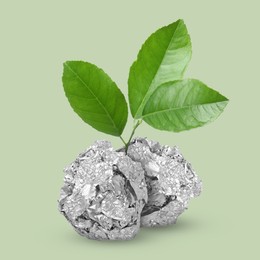 Image of Seedling with leaves growing from crumpled foil balls on light green background. Recycling