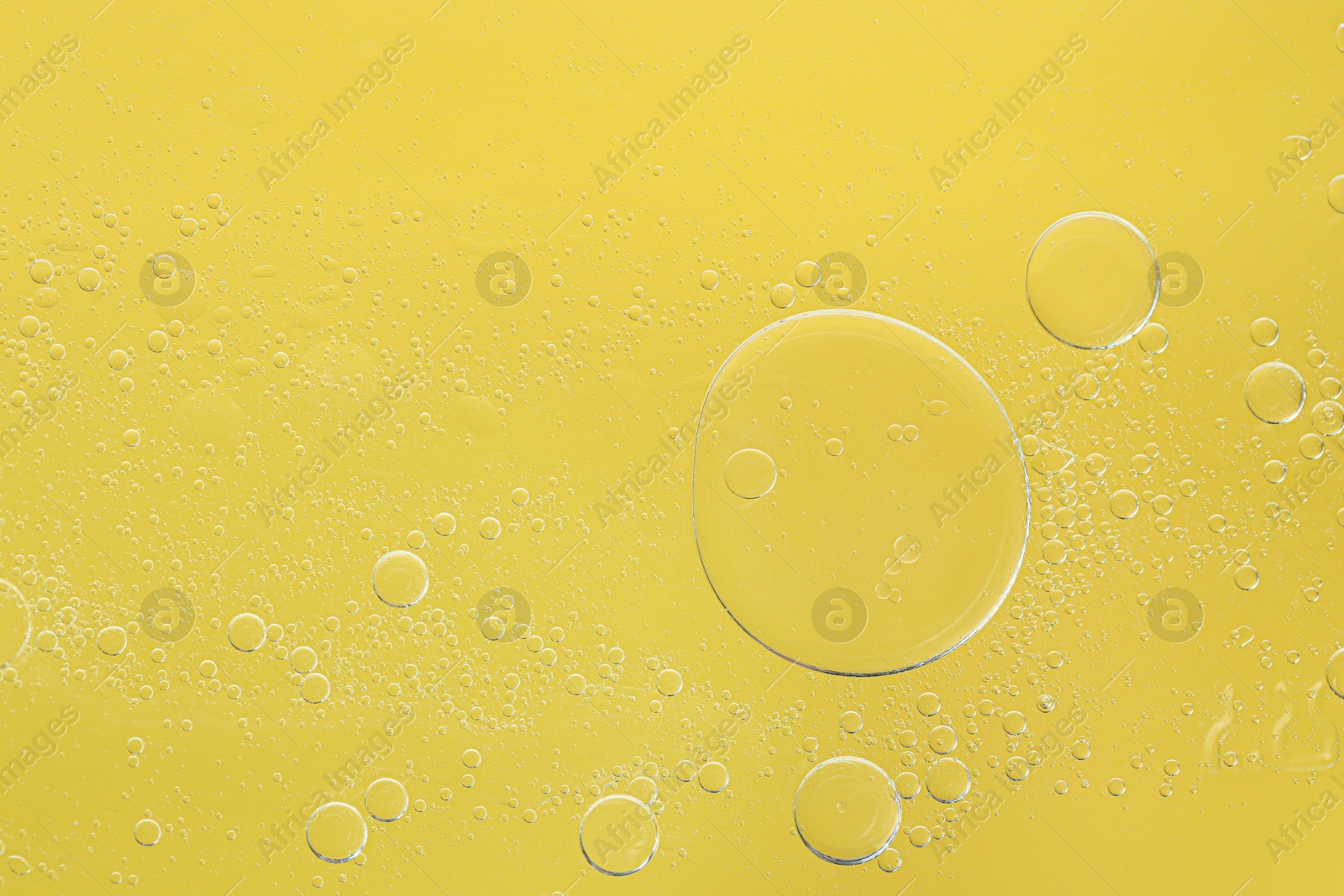 Photo of Essential oil bubbles on yellow background, macro view. Cosmetic product