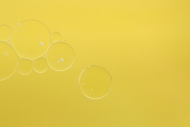 Photo of Cosmetic oil bubbles on yellow background, macro view. Space for text