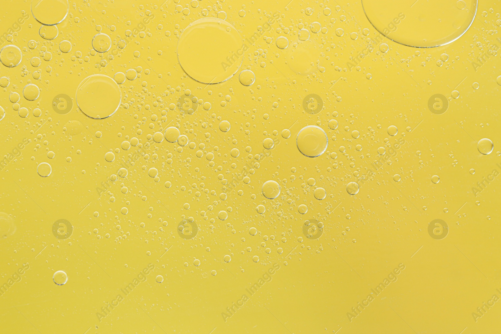 Photo of Essential oil bubbles on yellow background, macro view. Cosmetic product