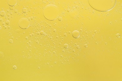 Essential oil bubbles on yellow background, macro view. Cosmetic product