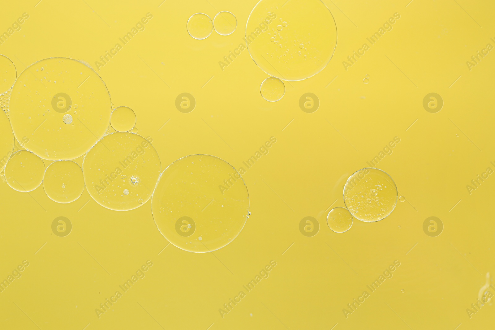 Photo of Essential oil bubbles on yellow background, macro view. Cosmetic product