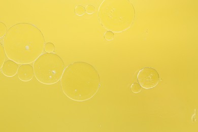 Photo of Essential oil bubbles on yellow background, macro view. Cosmetic product