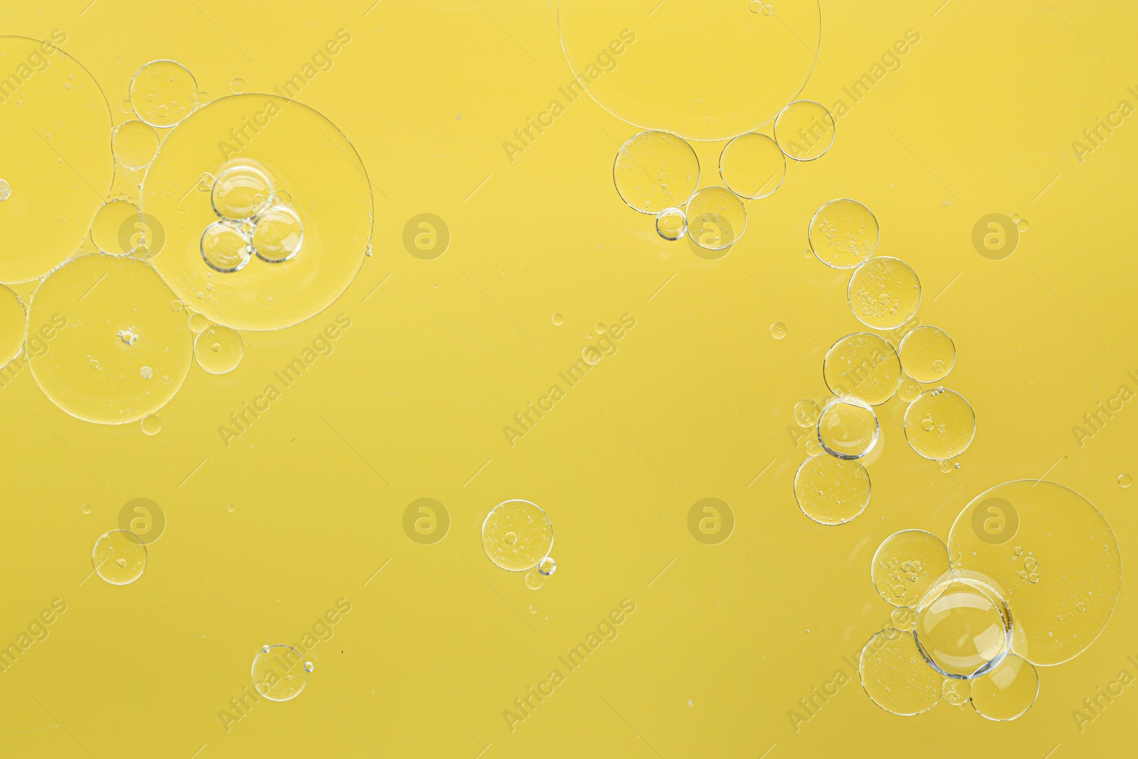 Photo of Essential oil bubbles on yellow background, macro view. Cosmetic product