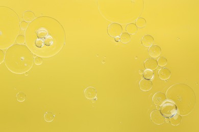 Essential oil bubbles on yellow background, macro view. Cosmetic product