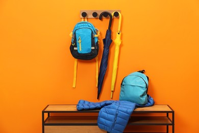 Photo of Colorful umbrellas, backpacks and jacket on wooden bench near orange wall