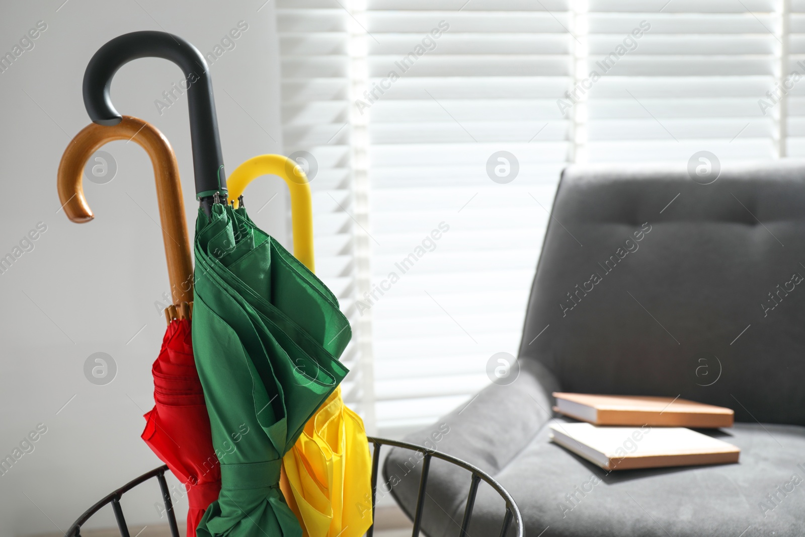 Photo of Colorful umbrellas in stand and armchair indoors, selective focus