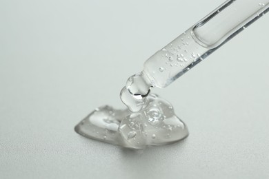 Photo of Dripping cosmetic serum from pipette on grey background, closeup