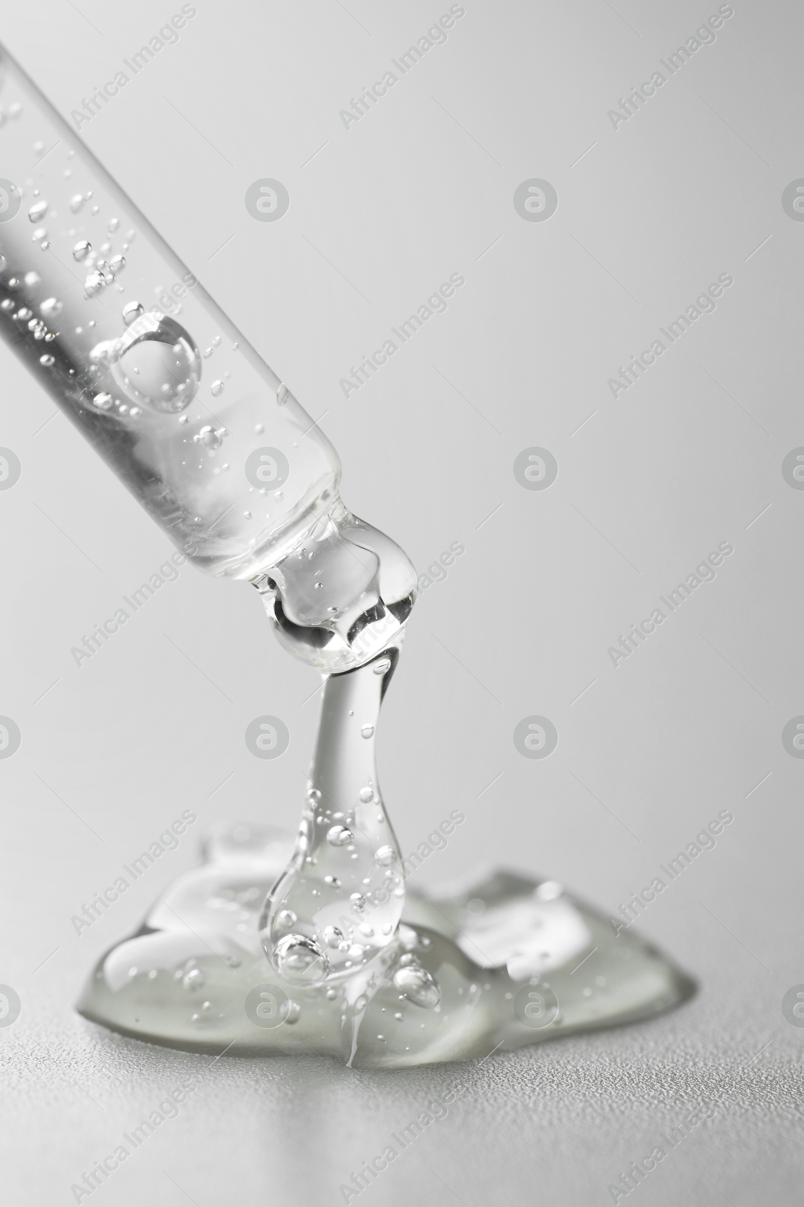 Photo of Dripping cosmetic serum from pipette on grey background, closeup