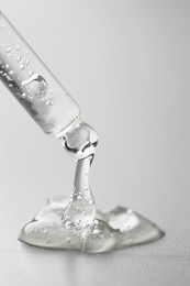 Dripping cosmetic serum from pipette on grey background, closeup