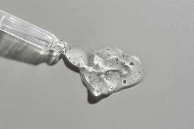 Dripping cosmetic serum from pipette on grey background, top view