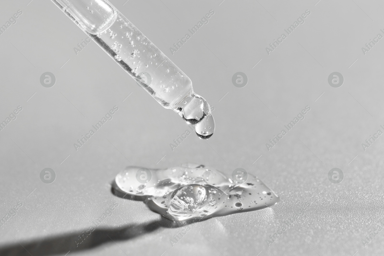 Photo of Dripping cosmetic serum from pipette on grey background, closeup