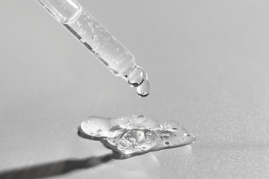 Dripping cosmetic serum from pipette on grey background, closeup