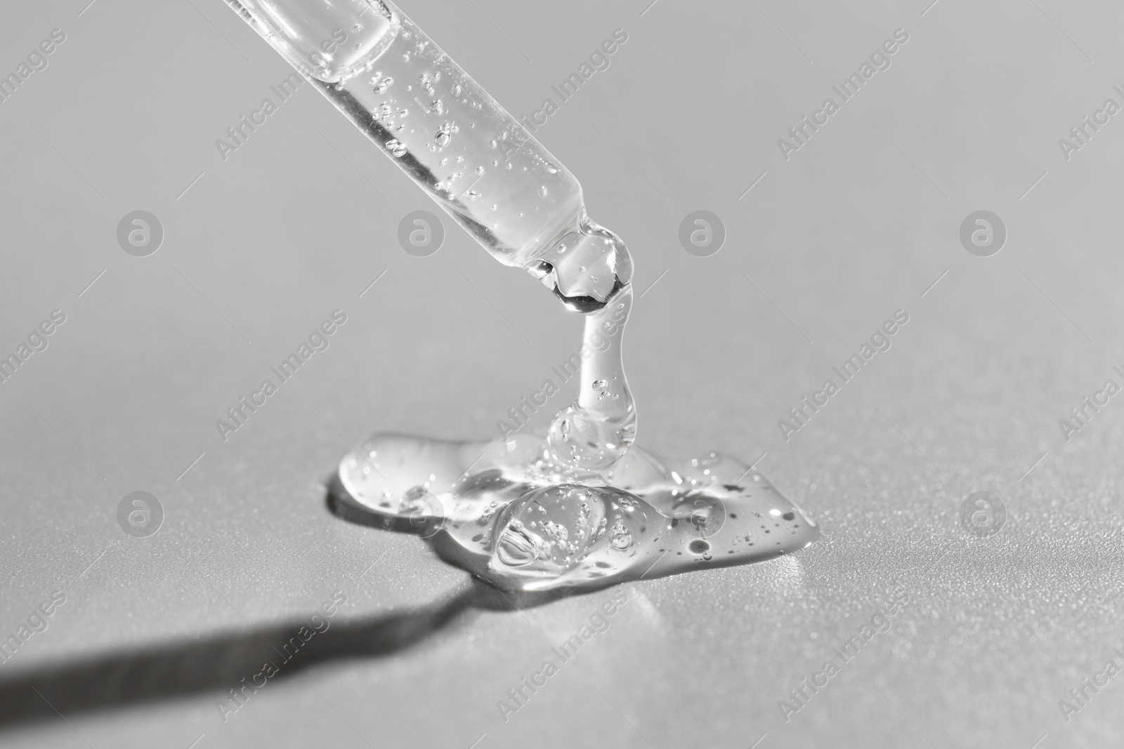 Photo of Dripping cosmetic serum from pipette on grey background, closeup