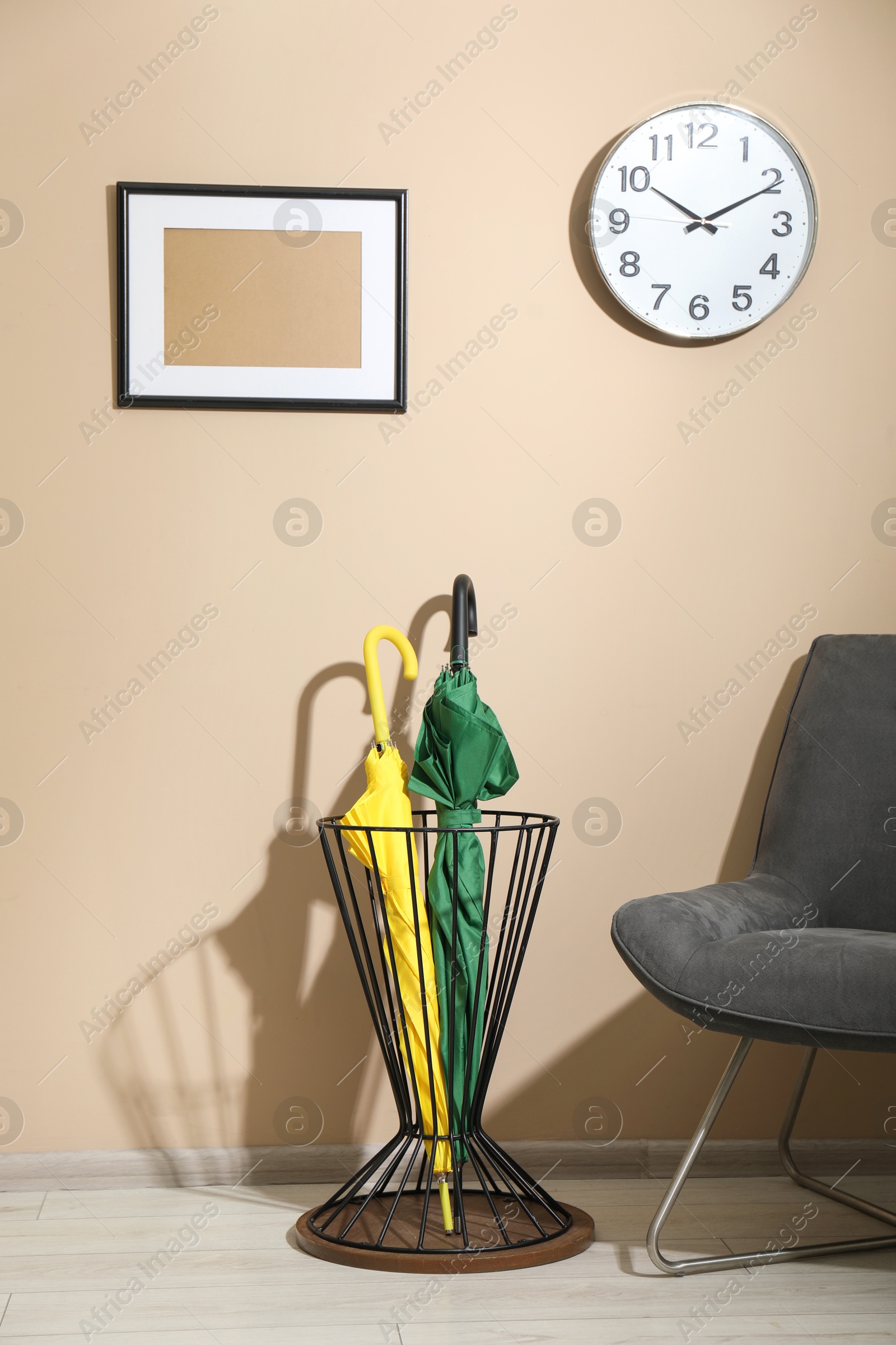 Photo of Bright umbrellas in holder and armchair near beige wall