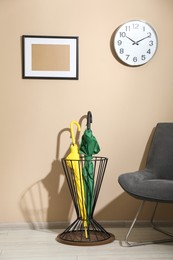 Photo of Bright umbrellas in holder and armchair near beige wall