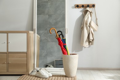 Photo of Holder with bright umbrellas, mirror and cabinets in hallway