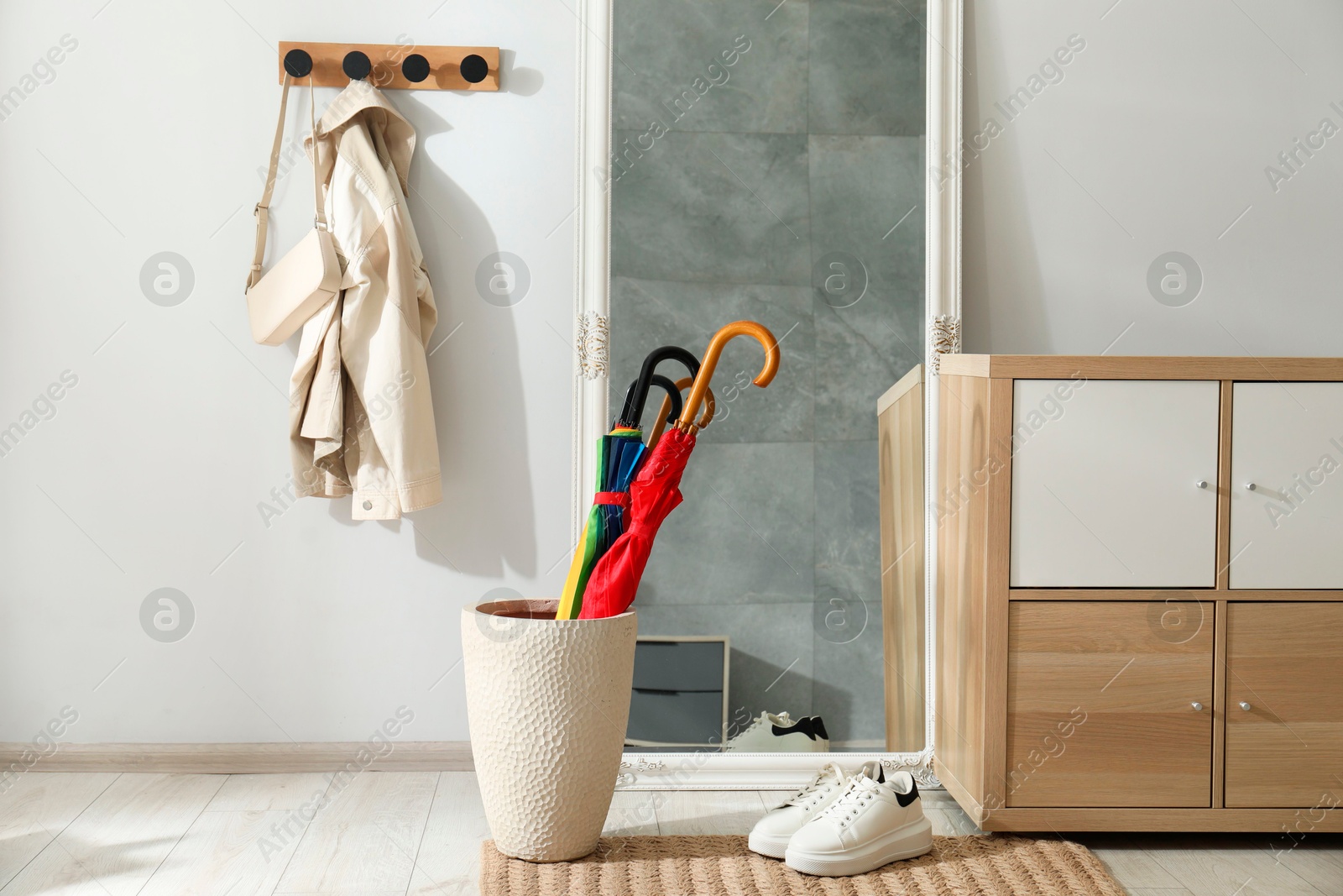 Photo of Holder with bright umbrellas, mirror and cabinets in hallway